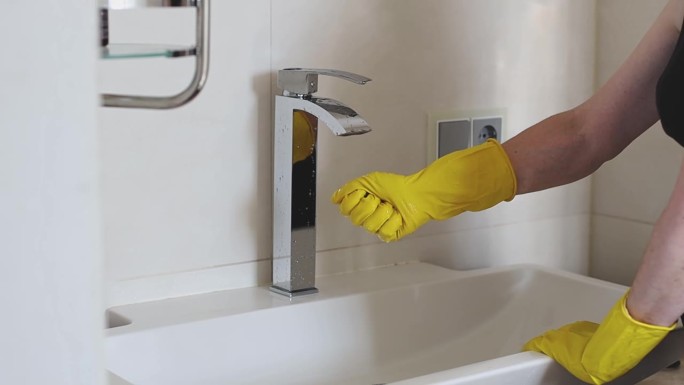 戴着黄色手套的清洁工的手从水中挤出一块海绵。