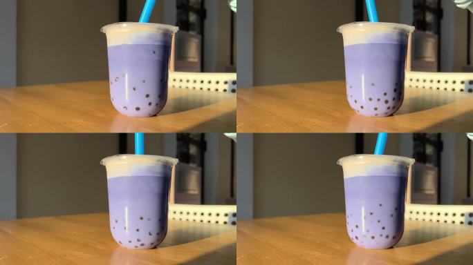 在一家餐厅的夏季露台上，用蓝色塑料吸管搅拌木桌上的蓝色丁香或紫色珍珠奶茶，背景是橙色米色的墙壁