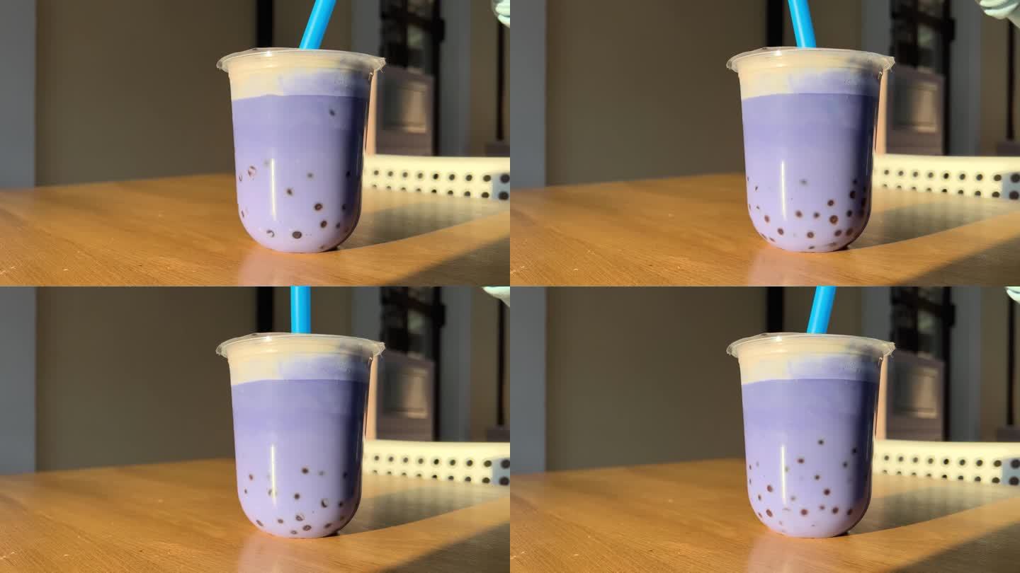 在一家餐厅的夏季露台上，用蓝色塑料吸管搅拌木桌上的蓝色丁香或紫色珍珠奶茶，背景是橙色米色的墙壁