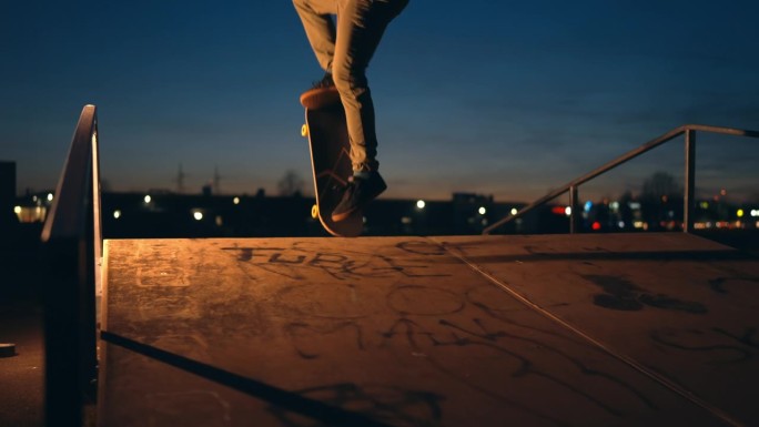 夜间在滑板公园用滑板表演分流的年轻人侧视图
