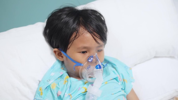 亚洲男孩躺在床上用吸入器治疗肺病。