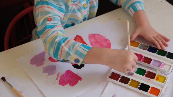 蹒跚学步的小女孩用水彩画，爱心贺卡。可爱幸福的家庭。孩子的艺术。工艺品，手工制作的概念。