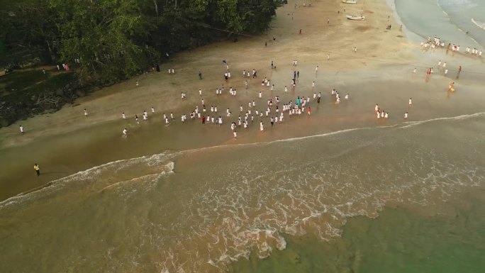 日落时分，身穿白色制服的学生在海边沙滩上玩耍的鸟瞰图。孩子们喜欢在海边夏令营，在浅浅的海浪中奔跑和欢