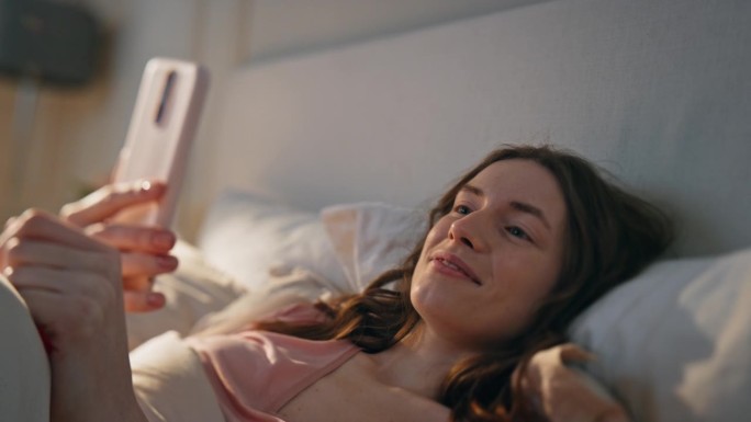 特写:放松的女孩在床上视频通话。正醒着，拿着手机的女人