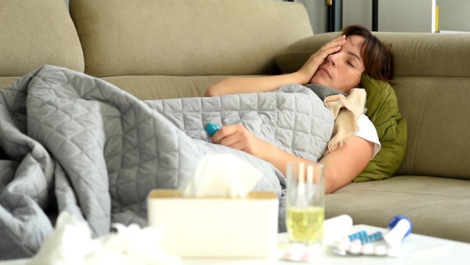 一位中年妇女躺在沙发上，发烧，发冷，有生病的迹象。