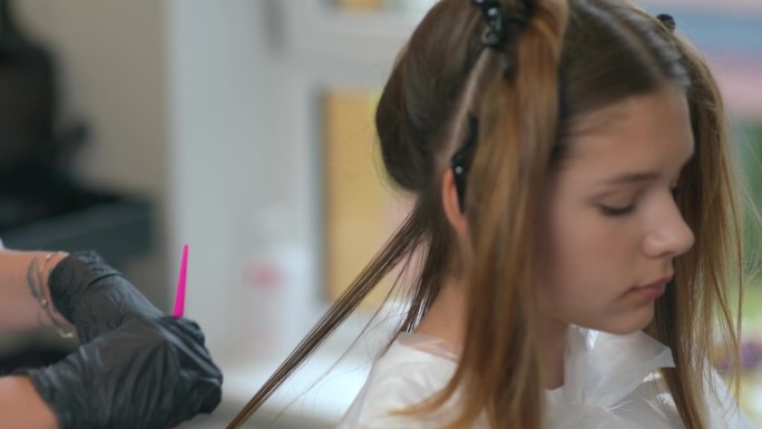 一位戴着黑色橡胶手套的女发型师正在用梳子为一位女顾客梳头。