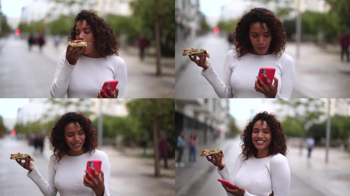 漂亮的拉丁裔女人边走边吃披萨边看她的智能手机。