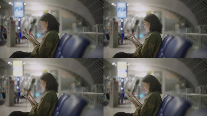 一名亚洲女子坐在机场登机口附近的候机区摆弄平板电脑。