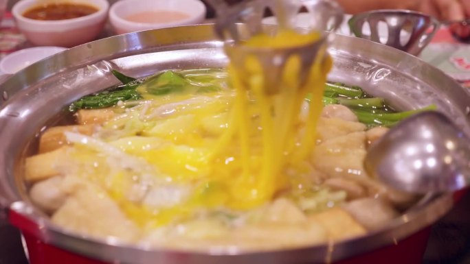 在泰国曼谷的一家餐馆里，在沸腾的热气腾腾的火锅里，将一些炒蛋淋在蘑菇和蔬菜上。