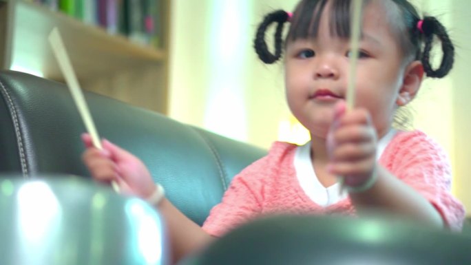 亚洲小女孩在家里的沙发上玩锅碗瓢盆。