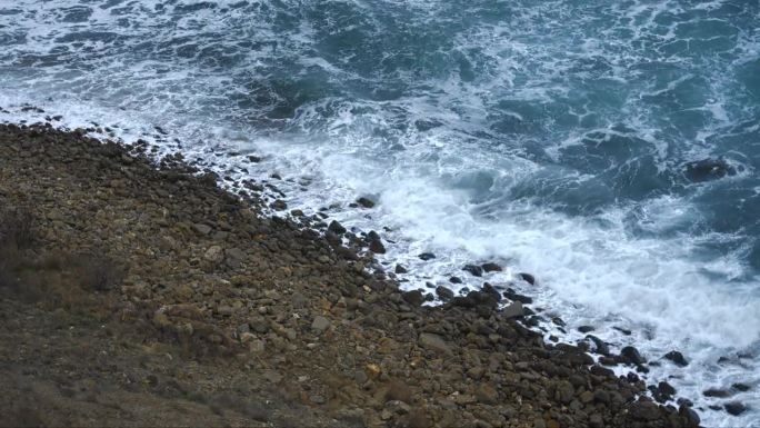 慢动作俯视图。蓝绿色的海浪和白色的泡沫在岩石海岸的冲浪线上。阴暗而美丽的海景。积极情绪的涌动