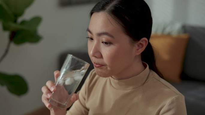 亚洲女性喝冰水，感觉牙齿敏感，坐在家里办公室。