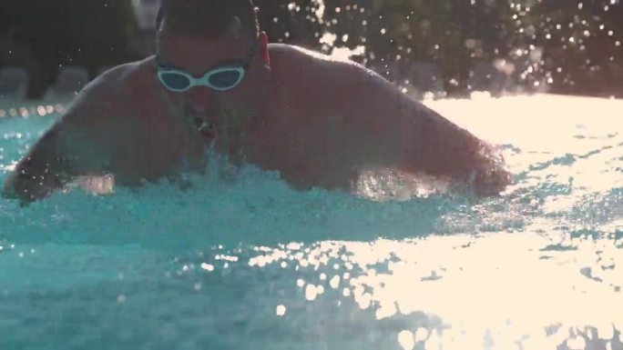 超级慢动作-时间扭曲效果男子完美蝶泳，熟练地通过水溅在健康俱乐部游泳池