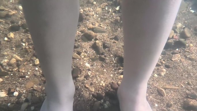 一个在水下行走的孩子的腿碰到了水下的沙子和岩石，阳光照了下来。