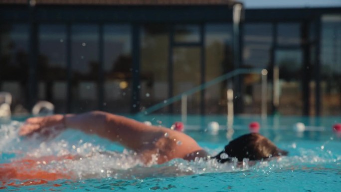 SLO MO男运动员戴着护目镜，在度假泳池清澈的蓝色水中练习蝶泳
