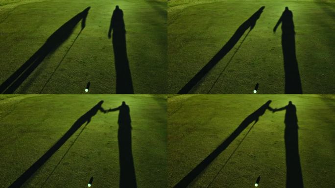 两个高尔夫球手在果岭和一个高尔夫球上握手的影子