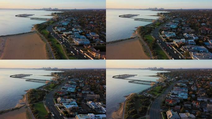 无人机视频飞过布莱顿的海滩和沿海道路，日落时墨尔本美丽的城市天际线在遥远的地平线上