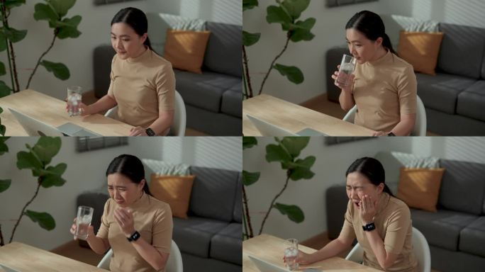 亚洲女性喝冰水，感觉牙齿敏感，坐在家里办公室。