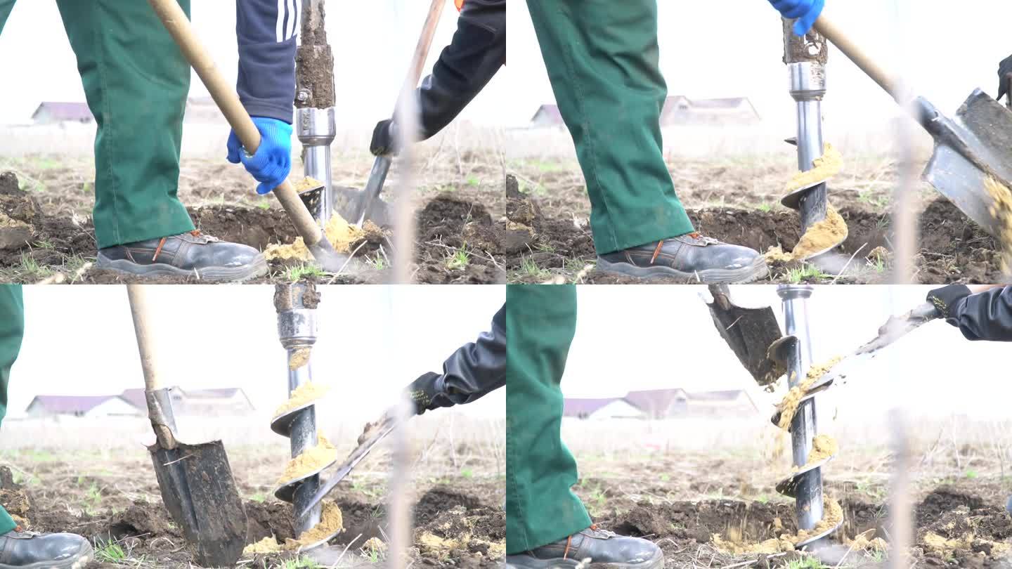 两名工人用铲子从沙子和泥土中清理大型钻机的画面