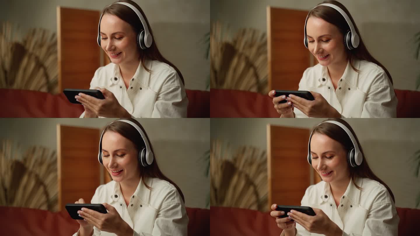 兴奋的年轻女子戴着耳机，在智能手机上玩在线游戏，网络直播。
