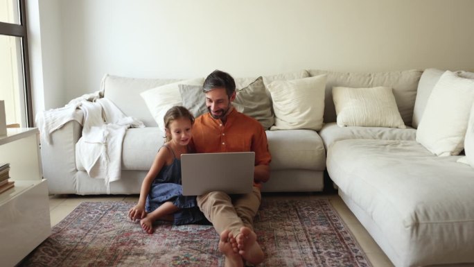 慈爱的父亲和女儿坐在地板上使用笔记本电脑