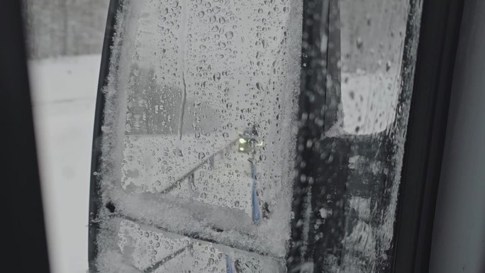 在暴风雨中，汽车的后视镜上覆盖着湿雪。后视镜反射出后面那辆车的前灯。