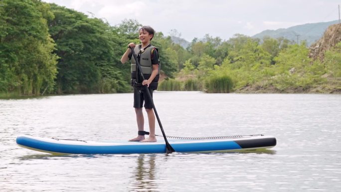 亚洲运动新秀在湖边学习玩桨板。暑假单人户外水上运动和旅游。