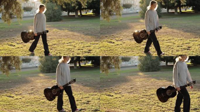 美丽的欧洲时髦吉他手女孩带着吉他走过阳光明媚的公园。一个十几岁的女孩欣赏着夏日的夕阳，穿过公园向前走