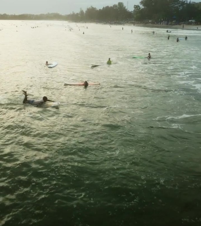 日落时海浪中的冲浪者鸟瞰图。密集的人群冲浪，在板上划桨，等待着海浪。充满活力的海景，在黄金时间从上面