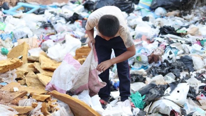 一个贫穷的男孩在郊区的垃圾填埋场收集垃圾。孩子们在这些工地工作以维持生计。贫困的概念。