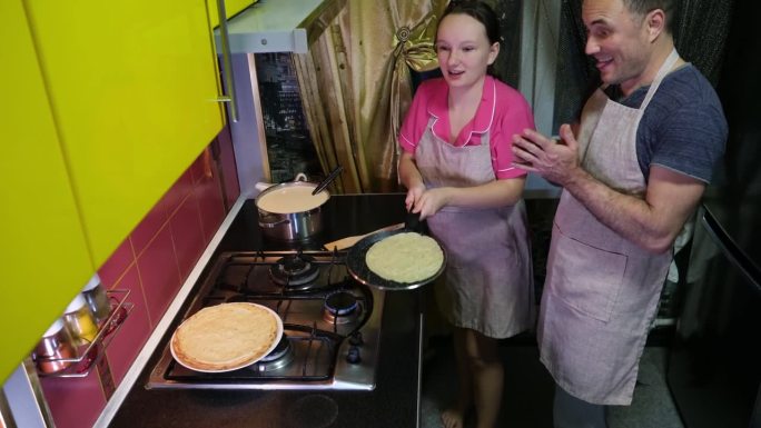 把煎饼扔在锅里十几岁的女孩和爸爸一起学习在煎锅里翻薄煎饼，煎煮晚餐早餐午餐相同的技巧家居陈设黄色厨房