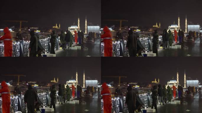手持拍摄的人们穿着雨衣，站在加拉塔桥上钓鱼，背景是蓝色的清真寺，夜晚在土耳其伊斯坦布尔