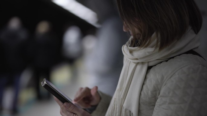 土耳其伊斯坦布尔，一名女子夜间在地铁站使用智能手机的侧视图