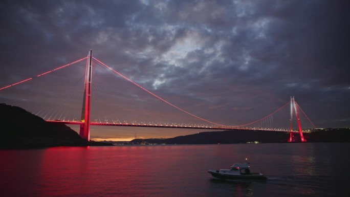 发光的Yavuz Sultan Selim大桥照亮了博斯普鲁斯海峡，而摩托艇在夜晚行驶