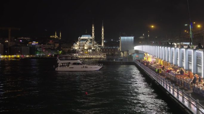 手持拍摄的游艇在马尔马拉海加拉塔大桥与蓝色清真寺照明在夜间在伊斯坦布尔，土耳其