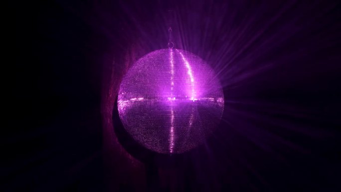舞会上有一个带镜子的迪斯科球在旋转。深红色、紫色和淡紫色的光线在烟雾中反射出来。