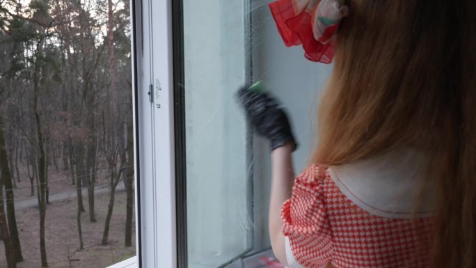 一个穿着红裙子打着蝴蝶结的女孩在擦窗户上的灰尘。
