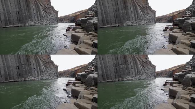 湍急的河流流经冰岛一个引人注目的玄武岩柱峡谷，展示了大自然的原始之美和地质奇观