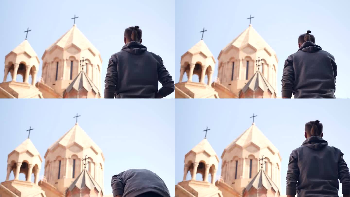 向后看:一个年轻的成年男子，留着时髦的发型，头顶扎着辫子，站在基督教教堂或寺庙的前面，按照传统，他在