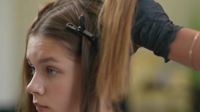 一个戴着发夹的女孩头部特写。一只戴着黑色橡胶手套的手取下了发夹。