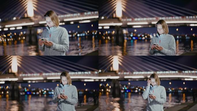 蓝色时刻，一名女子在博斯普鲁斯海峡边散步，用手机，背景是金角地铁大桥。
