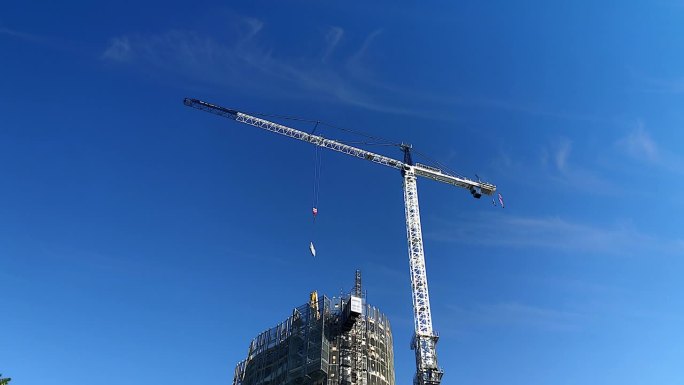 一台大型自爬式施工塔吊将设备吊到一栋正在施工的高层住宅楼上，云层吹过晴朗的蓝天