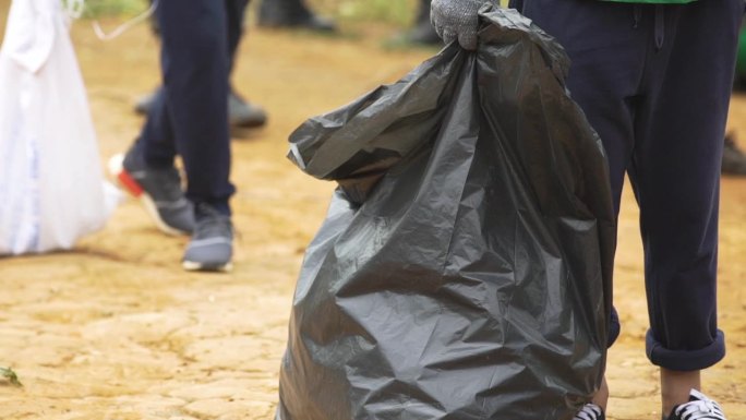 在公共场所收集垃圾的一名穿着运动鞋的女性志愿者的腿拿着黑色垃圾袋。