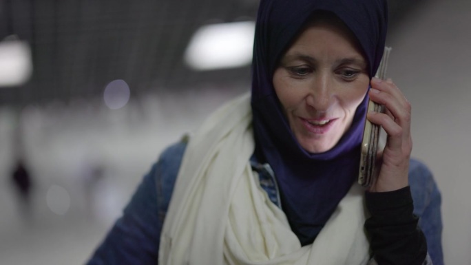 土耳其伊斯坦布尔地铁站的自动扶梯上，快乐的中年妇女手持智能手机聊天