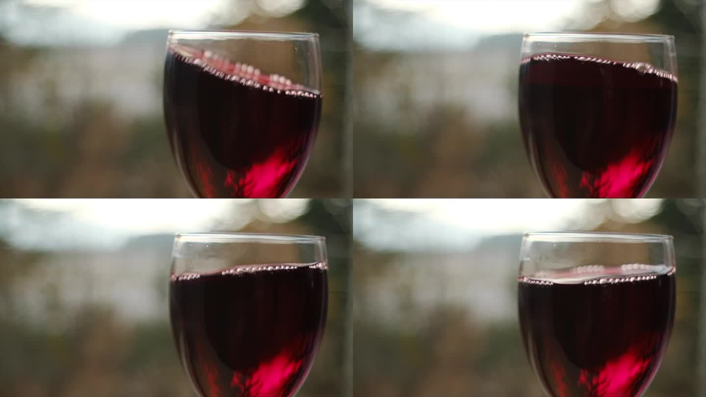 在自然的背景下，在阳光下摇曳着酒杯中的红酒。美丽的葡萄酒商业素材。高脚杯内的调酒过程特写。慢动作