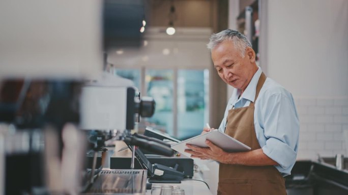 高级企业主在他的咖啡店里使用数码平板电脑和笔记本电脑