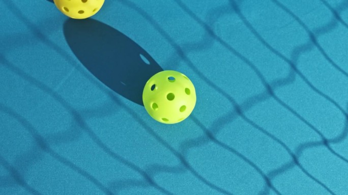 一个绿色的匹克球在蓝色的地板上被一个黄色的匹克球击中，网投下了阴影