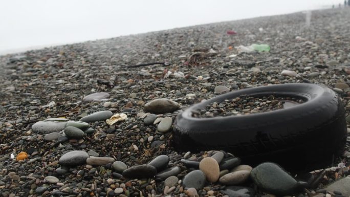 旧汽车轮胎在沙滩上的雾，湿的雪和雨的天气。塑料污染、垃圾和生态问题的危机观念。