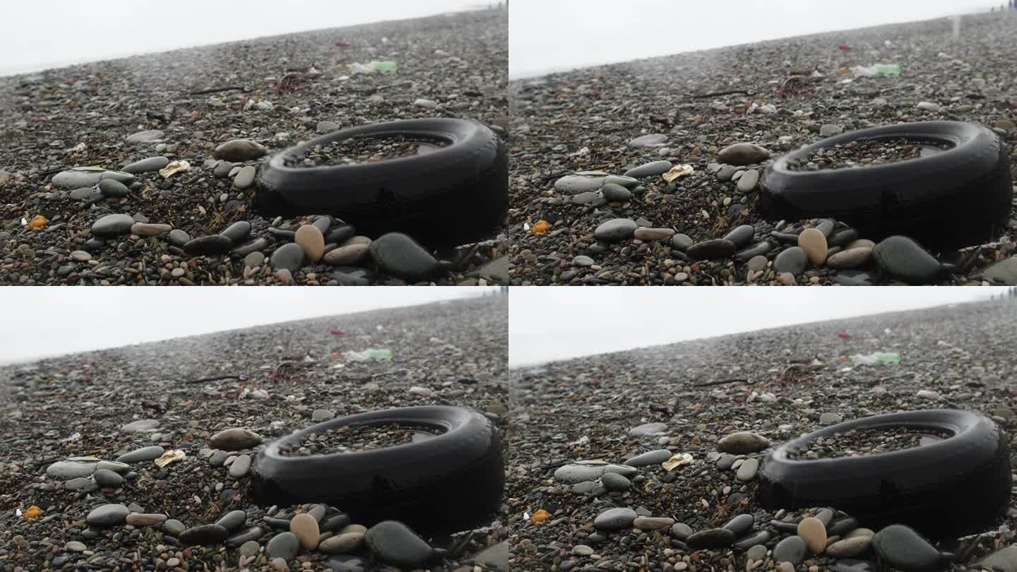 旧汽车轮胎在沙滩上的雾，湿的雪和雨的天气。塑料污染、垃圾和生态问题的危机观念。