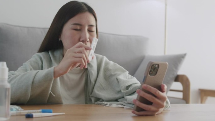 在COVID-19和冠状病毒大流行期间，一名亚洲妇女在家通过视频电话向朋友和家人展示快速抗原检测试剂